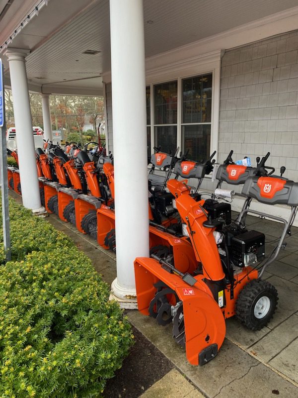 A row of orange snowblowers parked in front of a building.